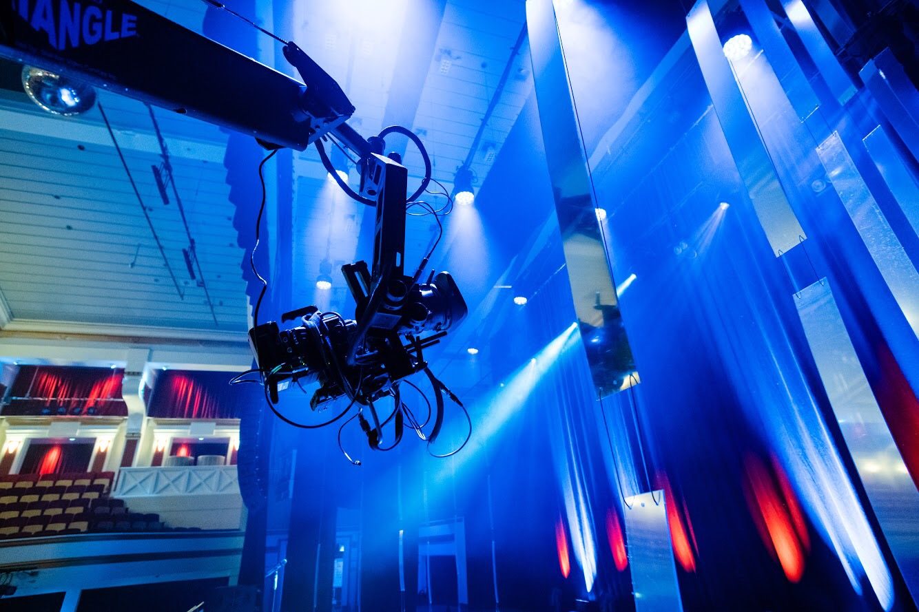 Camera on a jib arm above the stage in a theatre lit with blue and red light