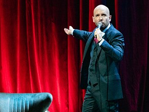 Comedian gesturing to the audience in front of red curtains